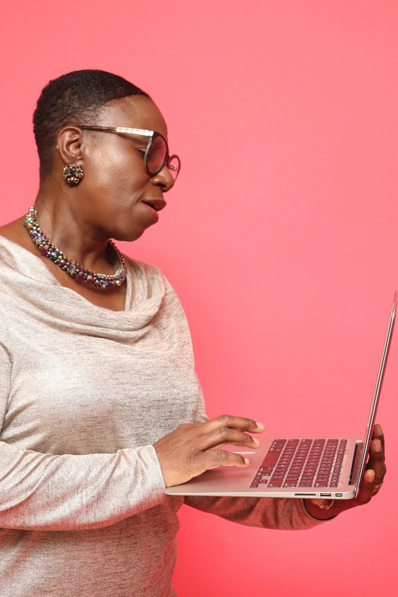 African American woman in front of a bright pink background holding a laptop